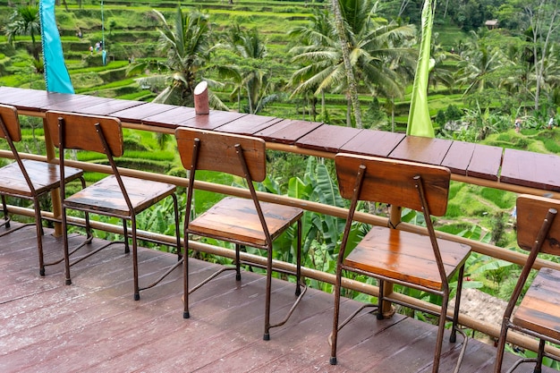 Wooden table and chairs in empty tropical cafe next to rice terraces in island Bali Indonesia