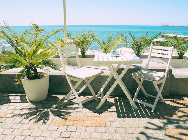 Tavolo e sedie in legno nella caffetteria all'aperto sul mare blu e sullo sfondo delle palme