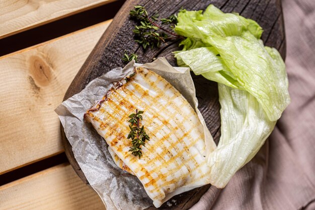 On a wooden table, cutting vintage board, on parchment paper, whole grilled squid with herbs