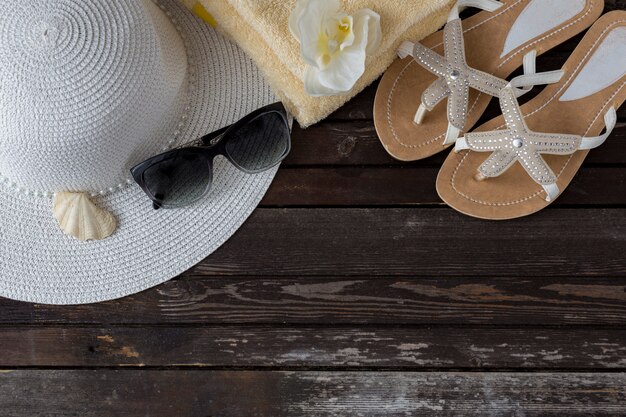 on a wooden table hat, flip-flops, sunglasses, towel, shell and orchid