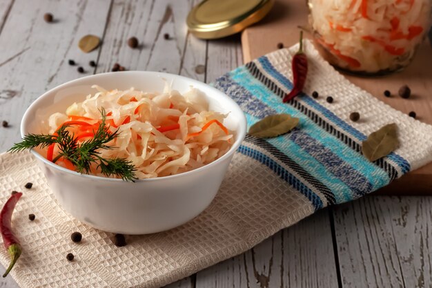 On a wooden table, sauerkraut with carrots and spices in a bowl. Horizontal top view, rustic style