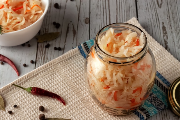 On a wooden table, sauerkraut with carrots and spices in a jar. Horizontal top view, rustic style