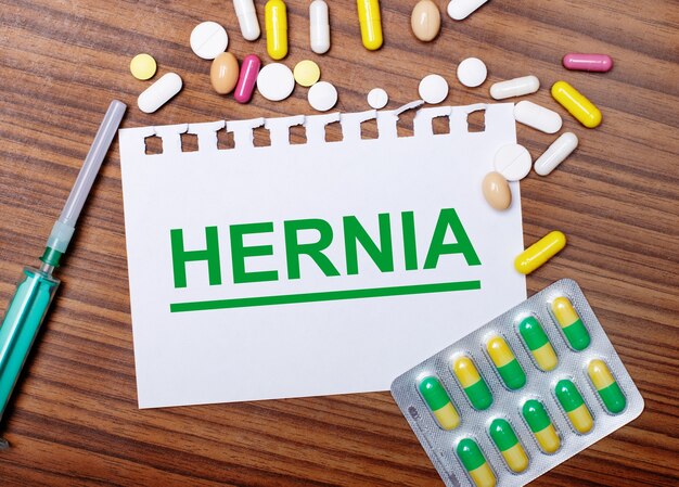 На деревянном столе шприц, таблетки и лист бумаги с надписью HERNIA.