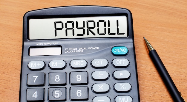 木製のテーブルには、黒いペンと「PAYROLL」というテキストの電卓があります。ビジネスコンセプト