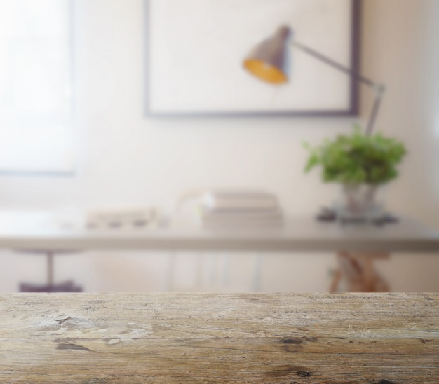 Wooden table top with blur of modern working table with book and lamp as background