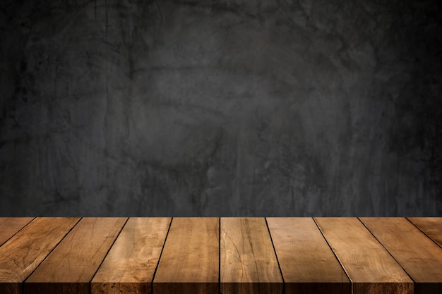 Wooden table top with dark concrete polished wall blurred background.