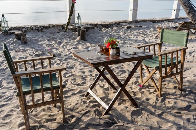 일몰 동안 열대 해변의 바다 근처에 있는 나무 테이블과 의자 2개 낭만적인 저녁 식사의 개념