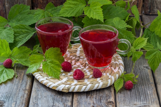 on a wooden table, two mugs of raspberry drink and raspberry berries 