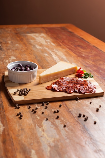 Wooden table with appetizer black olives, cheese, salami and black pepper