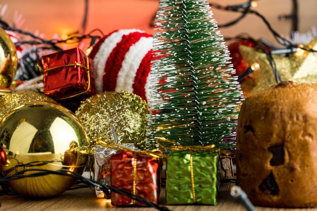 Wooden table with Christmas decorations. Red, silver and gold balls, gift boxes, lights, panettone, Christmas tree and others. Selective focus.