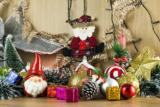 Wooden table with Christmas decorations. Red, silver and gold balls, gift boxes, lights, Santa Claus, Panettone, Christmas tree and others. Selective focus.