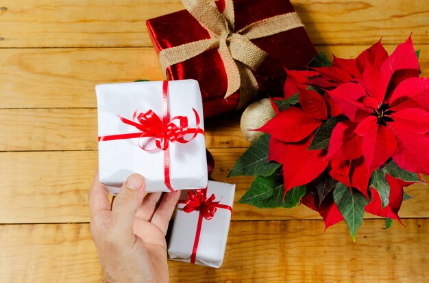 Wooden table with christmas gifts and poinsettia Person hands