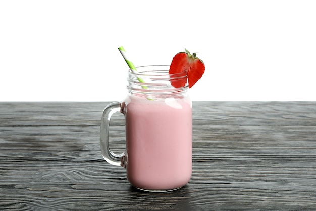 Wooden table with glass jar of strawberry milkshake isolated on white background