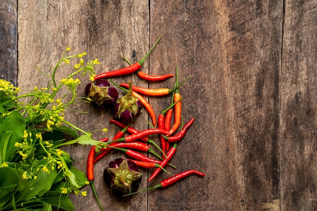 A wooden table with red chili peppers and a bunch of flowers.