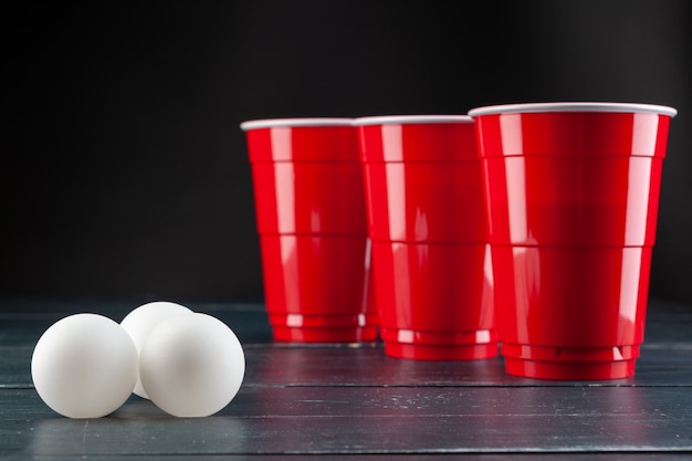 Wooden table with red cups and ball for beer pong