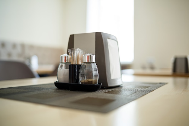 Photo wooden table with serving, salt and pepper, napkin holder, cup of black coffee