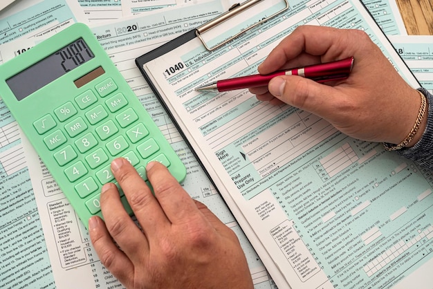 On a wooden table young male hands fill out tax form 1040 and make calculations on a calculator