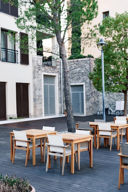 Wooden tables and chairs on a wood terrace in a street cafe near a stone house