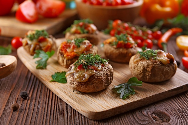 A wooden tablet with stuffed mushrooms and vegetables on the table