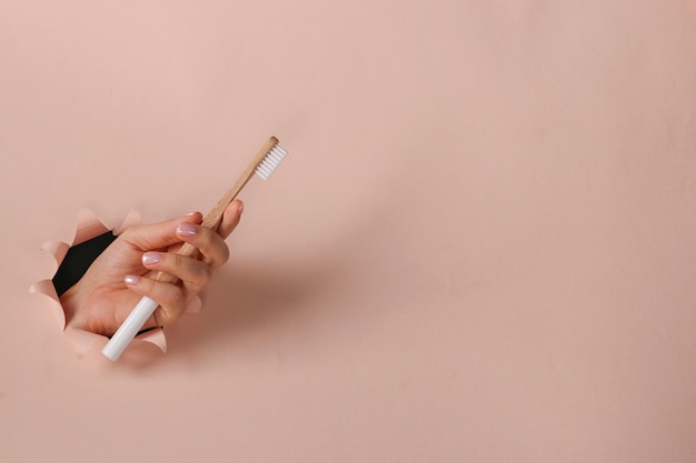 Wooden toothbrush in a female hand through round hole in pink paper