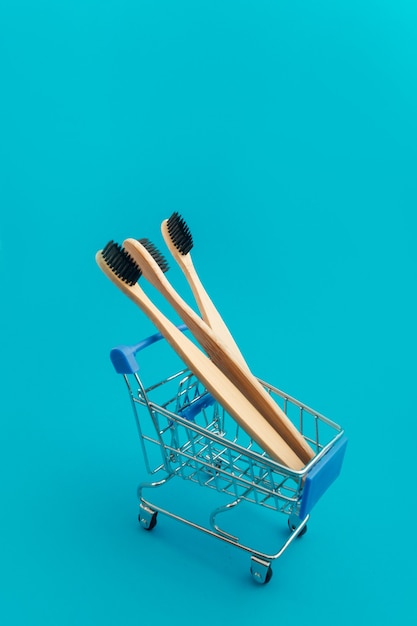 Wooden toothbrush in shopping cart on blue background