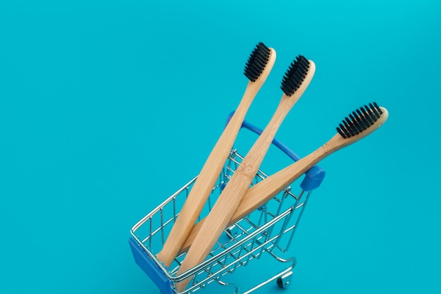 Wooden toothbrush in shopping cart on blue background