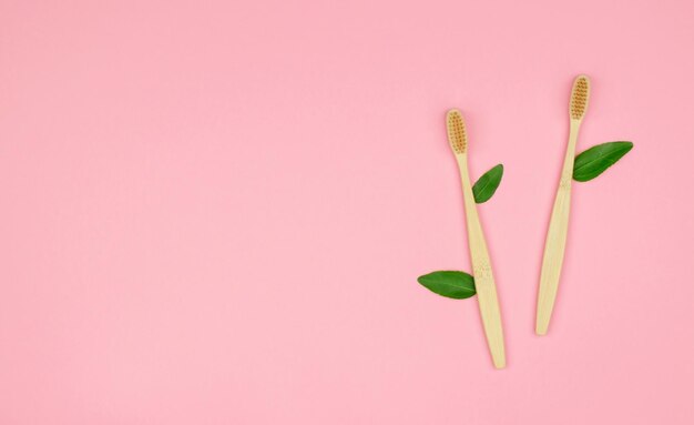 Wooden toothbrushes with green leaves on a pink background with place for text Ecofriendly products no waste and no plastic Zero waste Ecofriendly selfcare