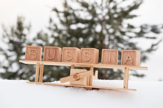 A wooden toy airplane in the snow against the background of a forest and the word Russia made up of cubes The concept of traveling to winter countries to Russia Retro style vintage