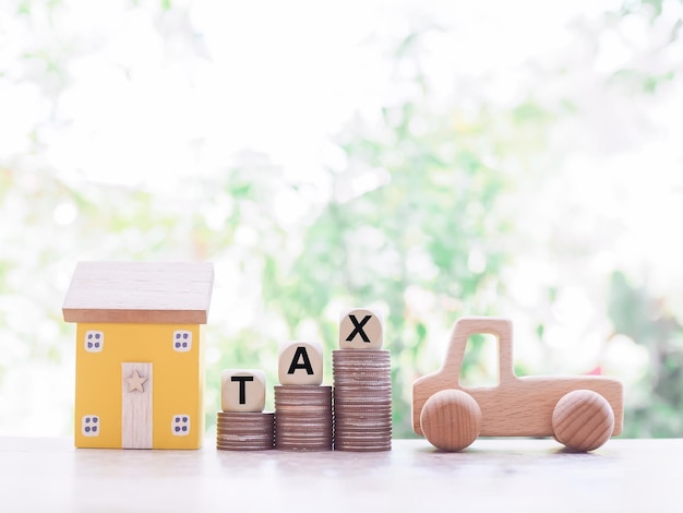 Wooden toy car Miniature house and wooden blocks with the word TAX on stack of coins The concept of paying tax for house or property and car