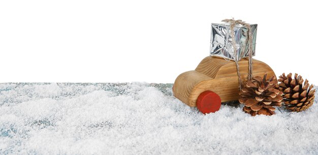흰색 표면 위에 눈 덮인 테이블에 선물 상자와 콘이 있는 나무 장난감 자동차