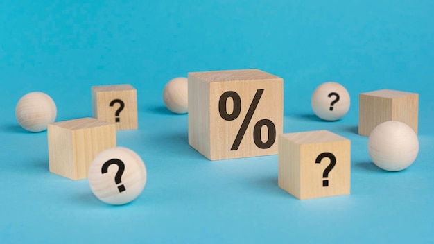 Wooden toy cube with a question marks viewed high angle on a blue background with wooden balls and cubes