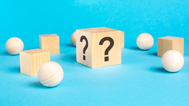 Wooden toy cube with a question marks viewed high angle on a\
blue background with wooden balls and cubes