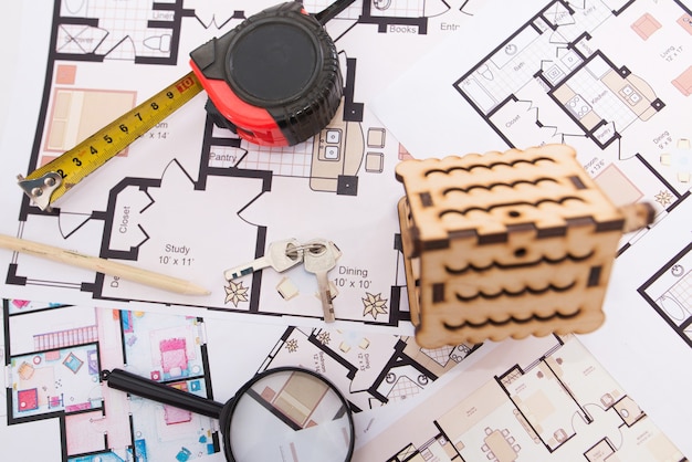 Foto casa giocattolo in legno, chiavi con metro a nastro e lente d'ingrandimento sulla pianta della casa.