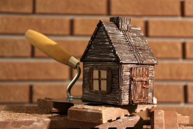 Wooden toy house on trowel and tiles on brick wall background