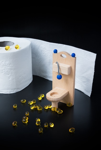 Wooden toy toilet, capsules and paper on black