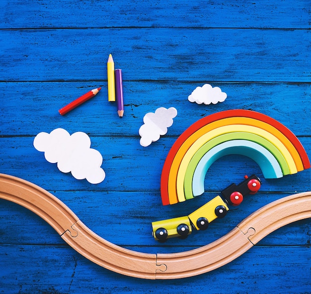 Wooden toy train railway for preschool child wood rainbow colored pencils on blue table Daycare kindergarten or montessori school background Kids dream Learn and Play concept