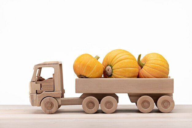 A wooden toy truck transports ripe pumpkins. White background, copy space.