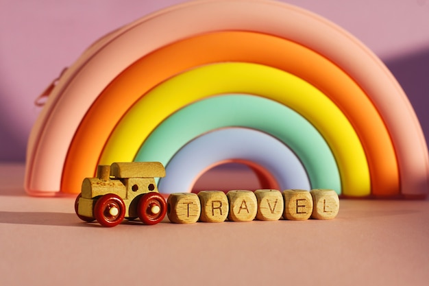 A wooden train with cubes with the inscription travel on the background of a voluminous bright rainbow