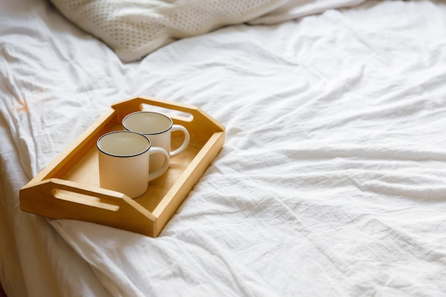 Фото Деревянный поднос и две белые кружки на кровати на белой простыне уютный утренний кофе в постель