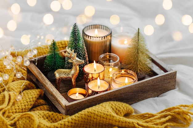 Wooden tray with burning candles  and christmas decorations on with warm plaid. Winter cozy style. Hygge concept.