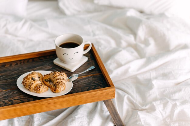 a wooden tray with croissants and cup of coffee on bed