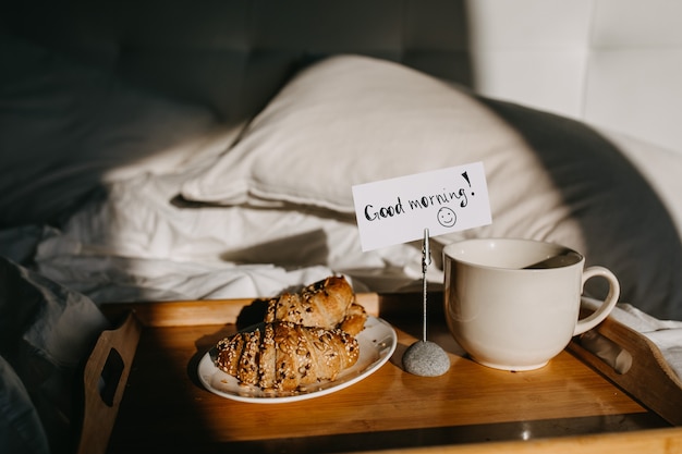 Photo a wooden tray with croissants and cup of coffee on bed
