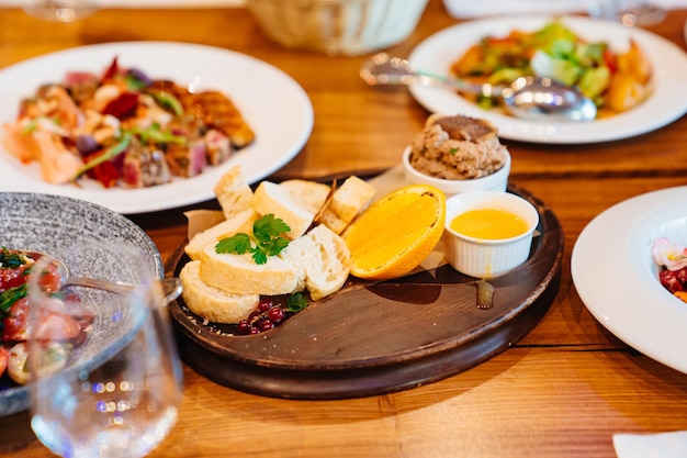 Деревянный поднос с паштетом и багетными тарелками с закусками на столе, который подается к празднику в ресторане, кейтеринг и доставка готовых домашних деликатесов для вечеринки