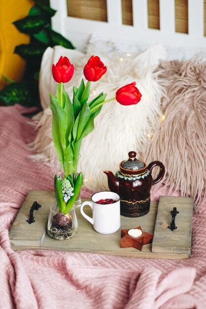 居心地の良いベッドの上にお茶とチューリップの花束が付いた木製トレイ、縦の写真。高品質の写真