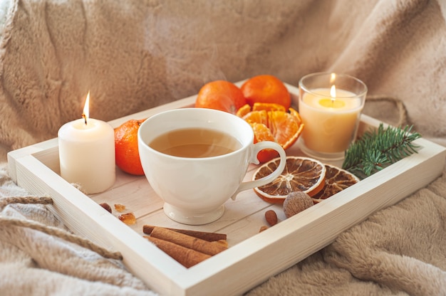 Un vassoio di legno con tè, mandarini, noci e spezie su un plaid beige. prima colazione invernale. il concetto di hygge. foto di alta qualità