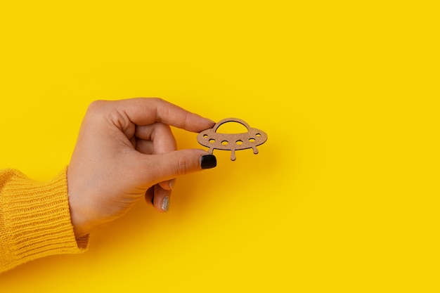 Wooden UFO in hand over yellow background