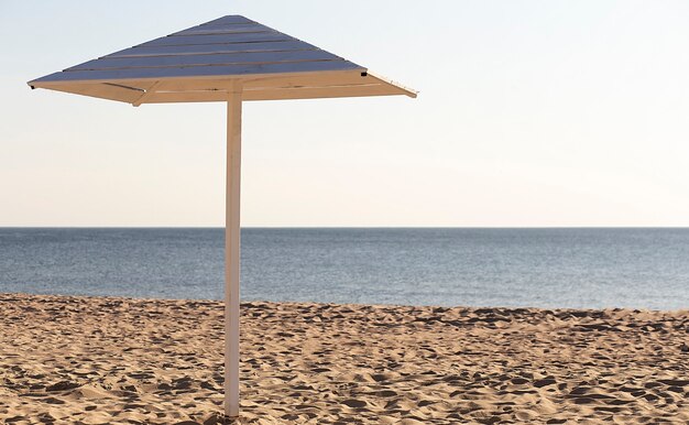 Деревянный зонт на красивом песчаном пляже, рядом с морем и голубым небом