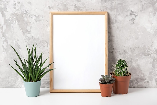 Wooden vertical frame with white blank card, and green houseplants flowers in pot on table on gray concrete wall background.