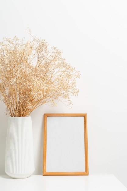 Wooden vertical frame with white vase of gypsophila flowers\
over white wall