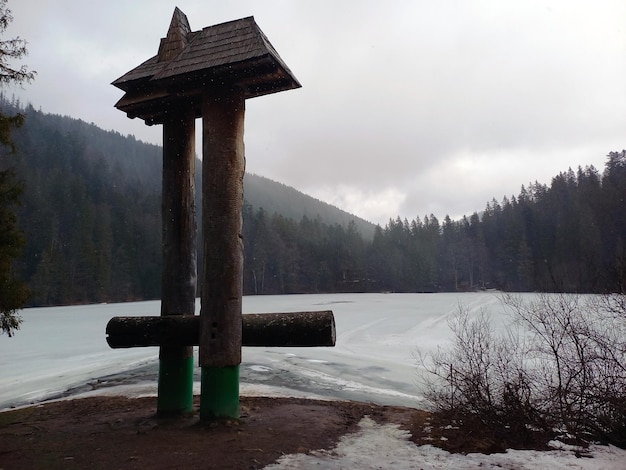 Деревянная винтажная скамейка в парке на берегу замерзшей реки напротив гор в пасмурную погоду.